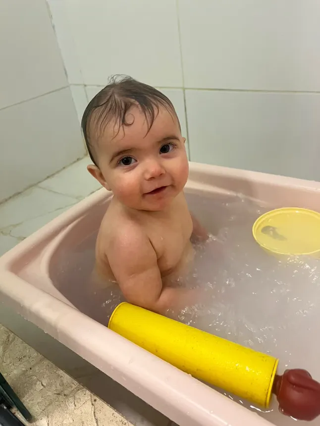 Joy sorrindo dentro da banheira, com brinquedos amarelos.